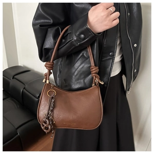 Detail of a brown crescent-shaped shoulder bag with decorative strap knot and matte PU leather