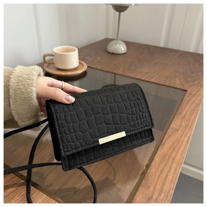 Detail of black crocodile texture bag with gold metal buckle on a minimalist wooden desk