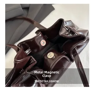 Detailed macro view of dual metal magnetic buckles on a dark brown glossy leather bag