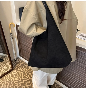 Rear view of a minimalist black frosted leather tote bag worn by a model in a cozy interior
