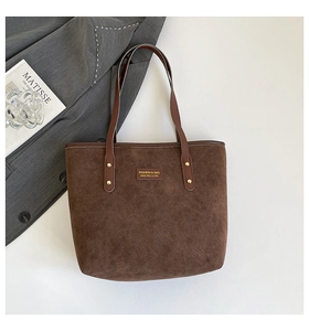 Close-up of suede tote bag with leather straps, rivets and logo tag in a chic studio setting
