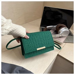 Detail of green crocodile texture flap bag with gold metal clasp on an office desk