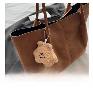 Détail d'un cabas en daim marron avec un joli charm d'ours en peluche sur l'anse