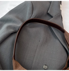 Detail view of the wide strap on a brown suede tote bag against a grey blazer