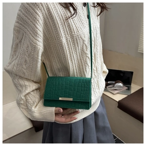 Detail of dark green crocodile pattern leather crossbody bag with gold metal clasp