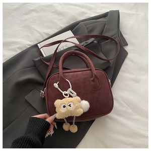 Detail of burgundy animal-patterned crossbody bag with a plush monster charm on it