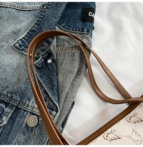 Detailed close-up of brown leather straps and swan print on the tote bag with denim jacket