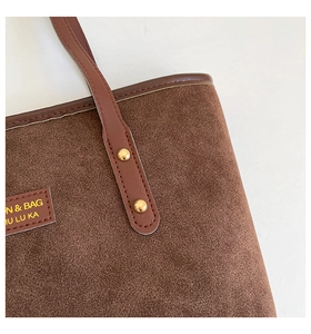 Close-up of coffee brown suede tote bag featuring metallic rivets and leather logo tag