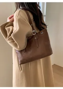 Dettaglio borsa tote in pelle marrone scuro con occhielli indossata su cappotto beige