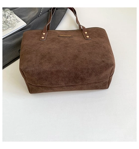 Detailed close-up of brown suede tote bag with leather handles and gold rivet accents