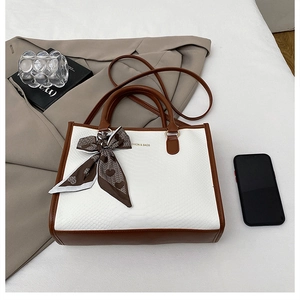 Detail of white crocodile pattern tote bag with brown leather handles and decorative scarf
