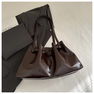 Detailed view of dark brown patent leather tote bag with pleats on black blazer background