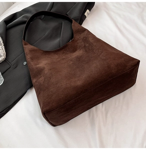 Flat lay of a large brown suede tote bag on white fabric with black blazer detail