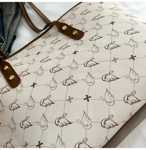 Detail of printed tote bag showing cream faux leather texture and brown leather handles