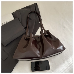 Detail of deep brown glossy patent leather tote with ruched texture and slim handles