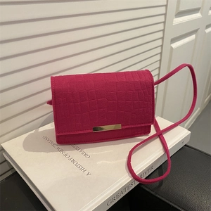 Magenta faux crocodile leather crossbody bag with gold metal buckle on white book