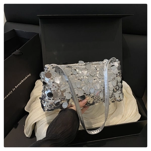 Close-up of a silver sequined shoulder bag with large round metallic discs in a gift box