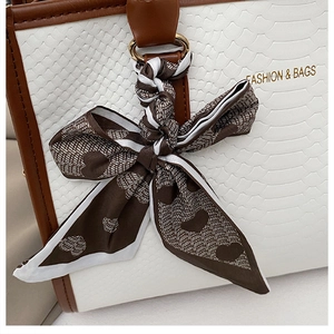 Détail d'un foulard en soie à motifs de cœurs noué sur un sac à main en texture serpent blanc