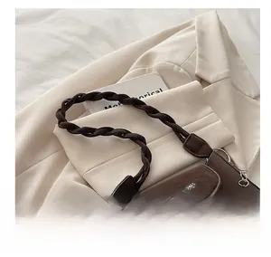 Detail of dark brown leather shoulder bag with woven strap and floral metal chain