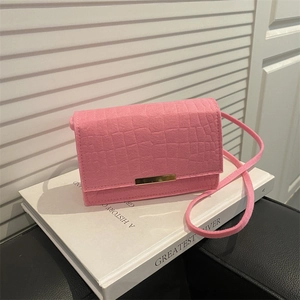 Pink crocodile texture shoulder bag with gold metal clasp on a white book
