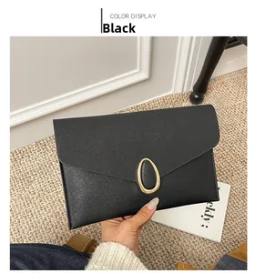 Detail of black Saffiano leather clutch bag featuring a prominent gold oval metal clasp