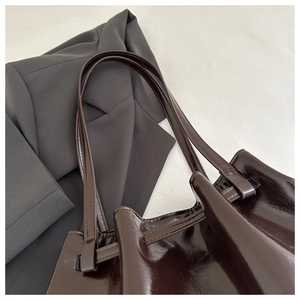 Detail of burgundy patent leather tote bag showing glossy texture and strap on a blazer
