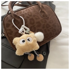 Close-up of a yellow plush monster charm with big eyes hanging on a leopard print bag