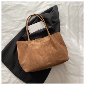 Détail du grand sac cabas en daim marron caramel sur un blazer et un livre d'art