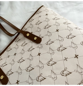 Close-up of beige tote bag with swan pattern, textured fabric and gold rivet details