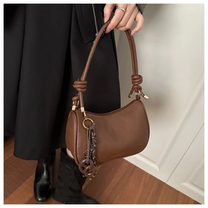 Close-up of brown textured leather shoulder bag with knot handle and golden hardware details