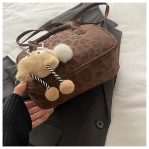 Detail of leopard print crossbody bag with plush monster charm on dark blazer