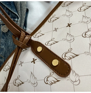 Close-up of premium tote bag featuring brown swan print and gold rivet leather handle