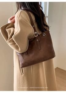 Brown retro tote bag with metal eyelets worn with a beige coat in a minimalist setting