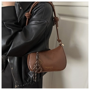 Detail of a brown leather crescent bag with knot strap and geometric metal pendant