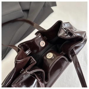 Detail of deep brown pleated tote bag featuring magnetic closure and glossy PU leather texture