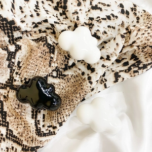 Detail of 3D cloud-shaped phone grips in black and white glossy finish on silk fabric