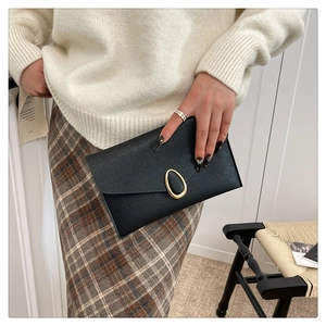 Detail view of a black Saffiano leather envelope clutch with a gold oval metal buckle clasp