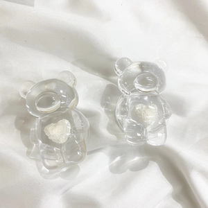 Detail of two transparent bear-shaped phone grips with white 3D hearts on white fabric