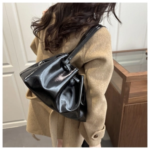 Detail of black glossy pleated underarm bag with oil wax leather texture on shoulder