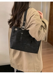 Detailed side view of minimalist black matte tote bag worn with a khaki trench coat