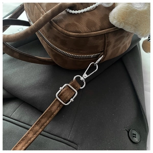 Close-up of brown suede crossbody bag with silver buckles and plush charm accessory