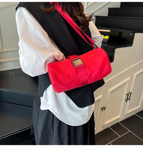 Detail of red cylindrical nylon shoulder bag featuring a black metal buckle and strap
