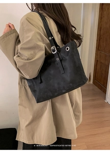 Dettaglio borsa tote nera opaca con occhielli argentati e tracolla su trench beige