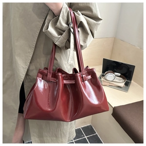 Close-up of burgundy pleated bucket bag with glossy finish shown in office setting