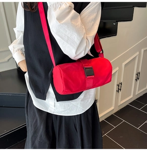 Detail view of a red cylindrical crossbody bag with buckle fastener and durable nylon strap