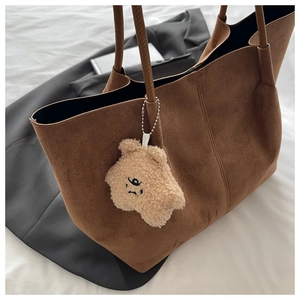 Détail d'un cabas en daim marron avec pendentif ours en peluche sur tissu blanc