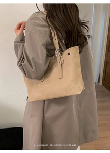 Detail of beige large tote bag showing metal eyelet accents and adjustable strap on model