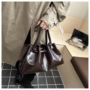Detail of dark brown glossy patent leather handbag with pleated texture and drawstring