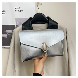 Detail of silver envelope clutch featuring brushed metallic texture and gold oval buckle