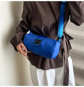 Blue cylindrical nylon crossbody travel bag with buckle detail shown on a model